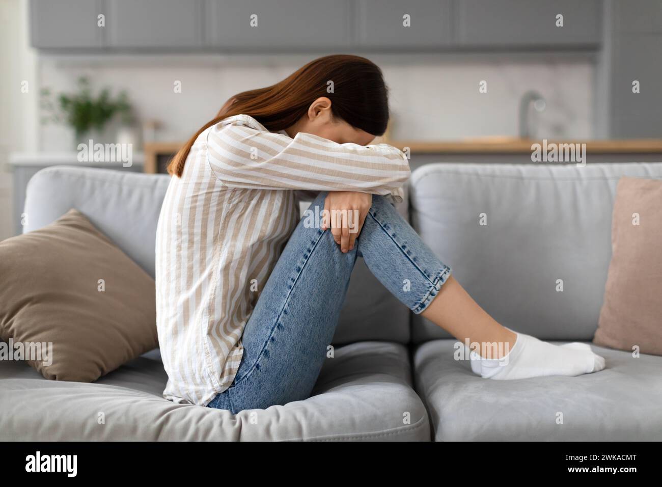 Upset young woman sitting on the sofa with her head down, side view Stock Photo