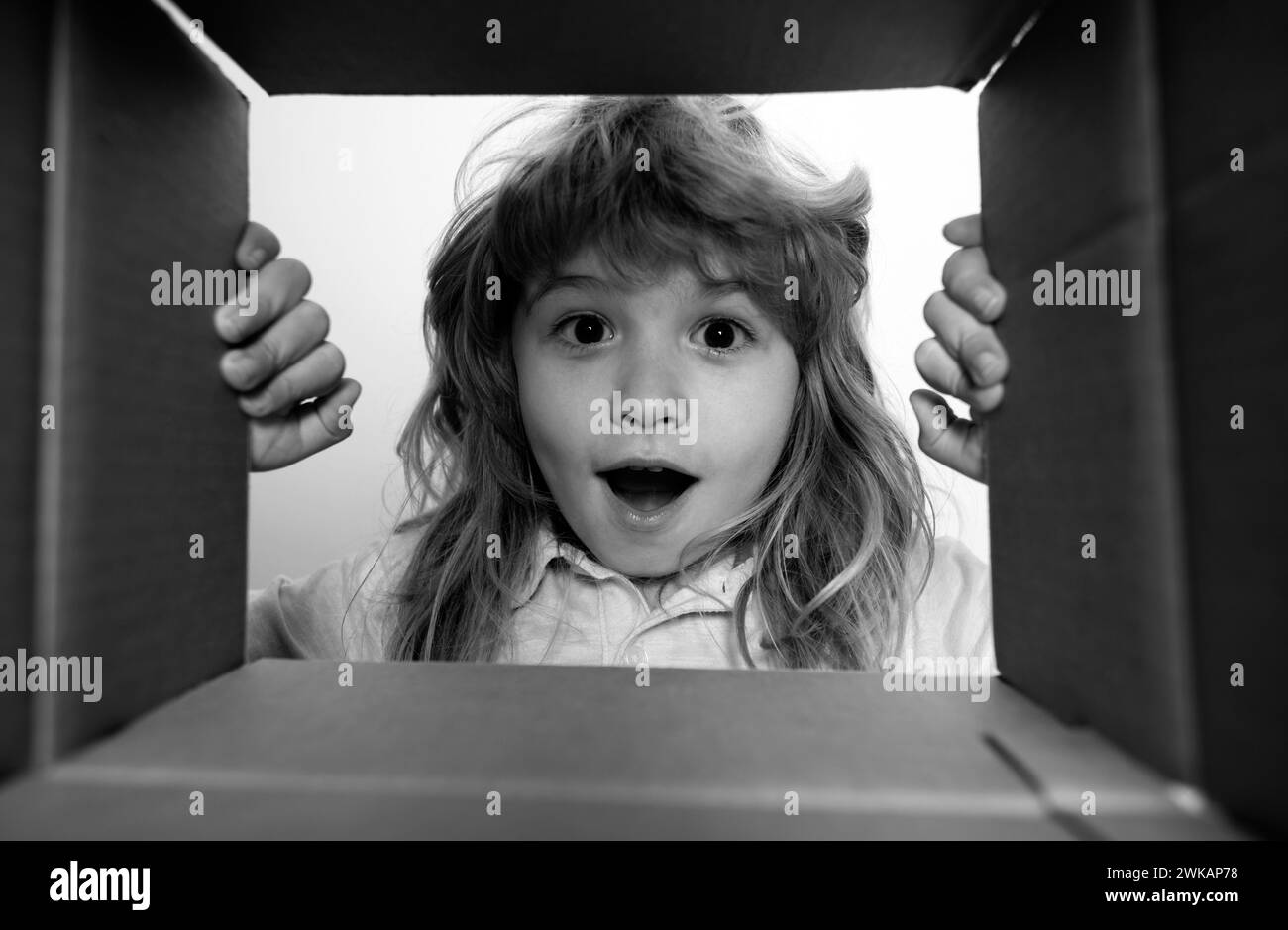 Unpacking cardboard box for kids. Happy little child boy is opening gift and looking inside cardboard box. Stock Photo