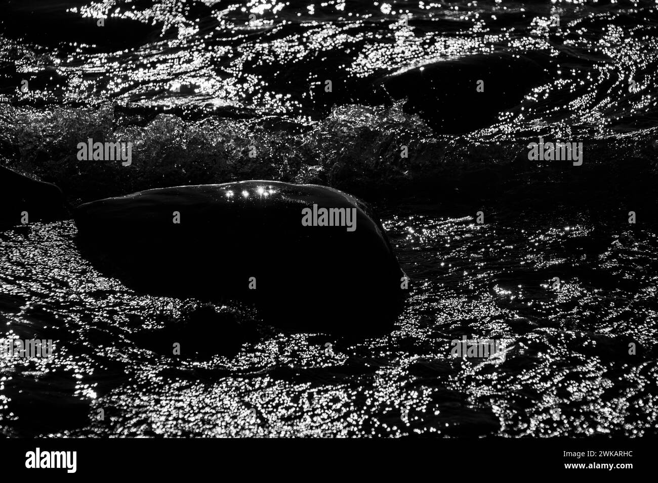 A boulder surrounded by sun reflections breaks up the surf on