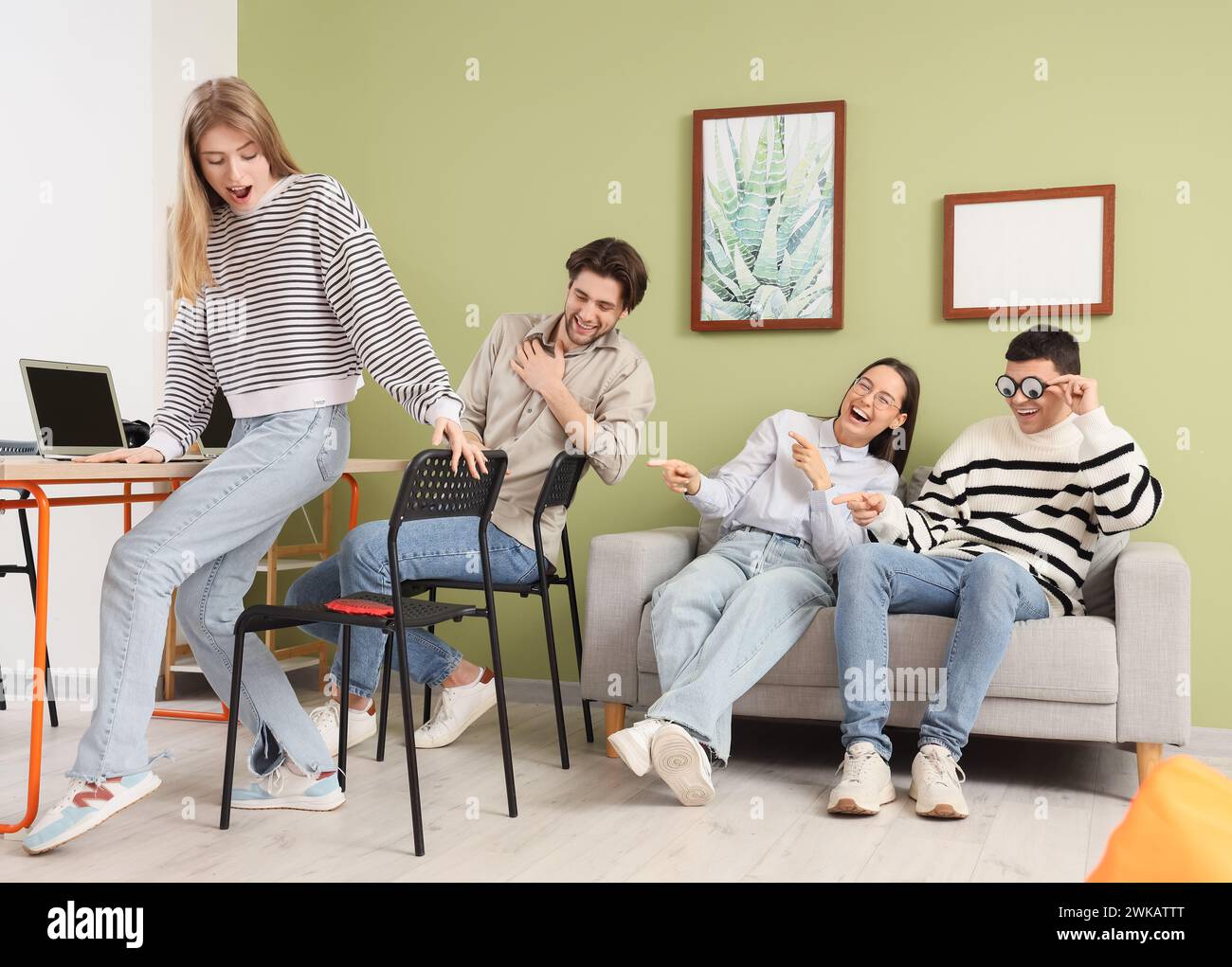 Young people laughing at their colleague sitting on whoopee cushion in