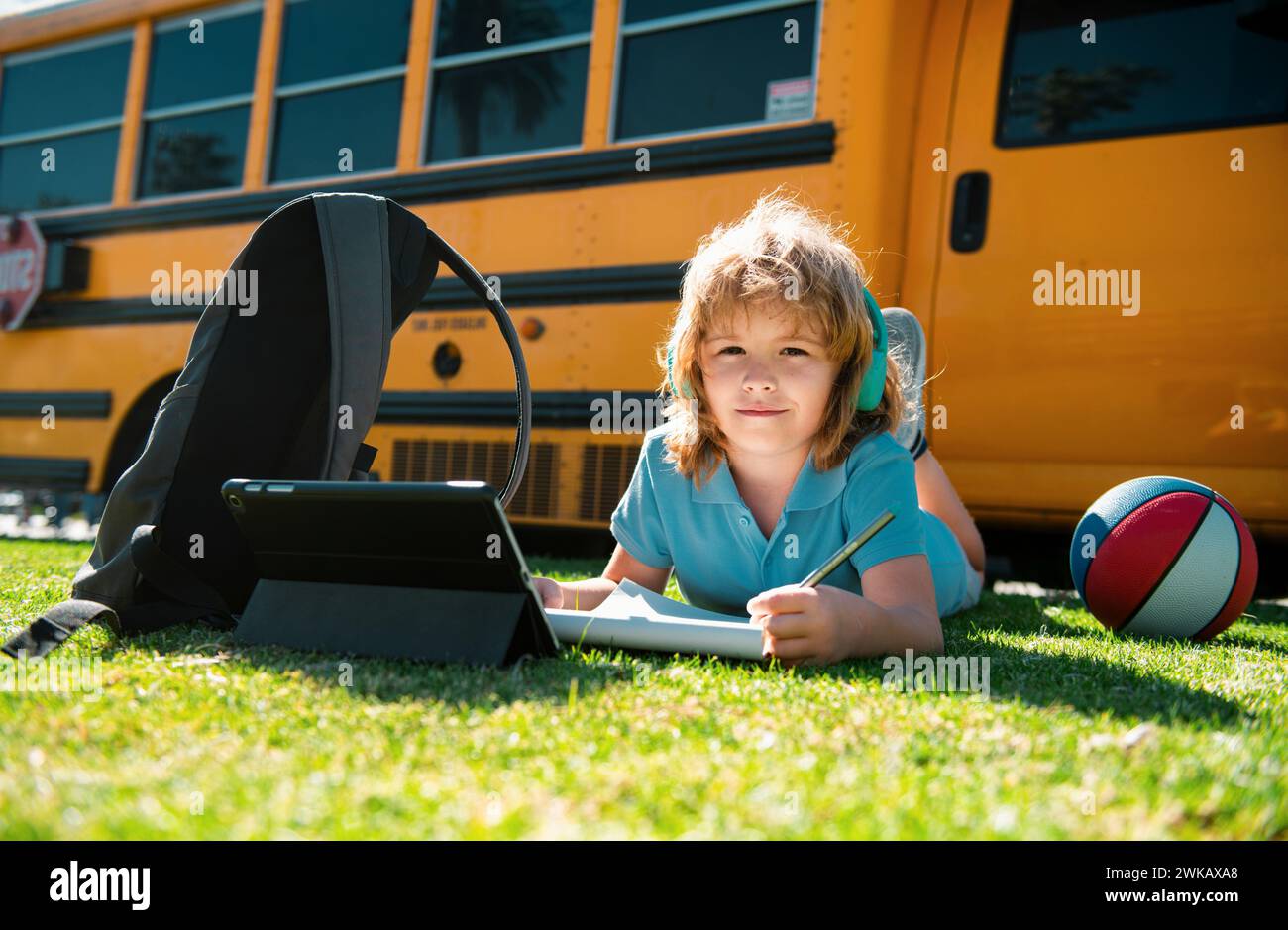 Child pupil does school homework laying on grass in the park near ...