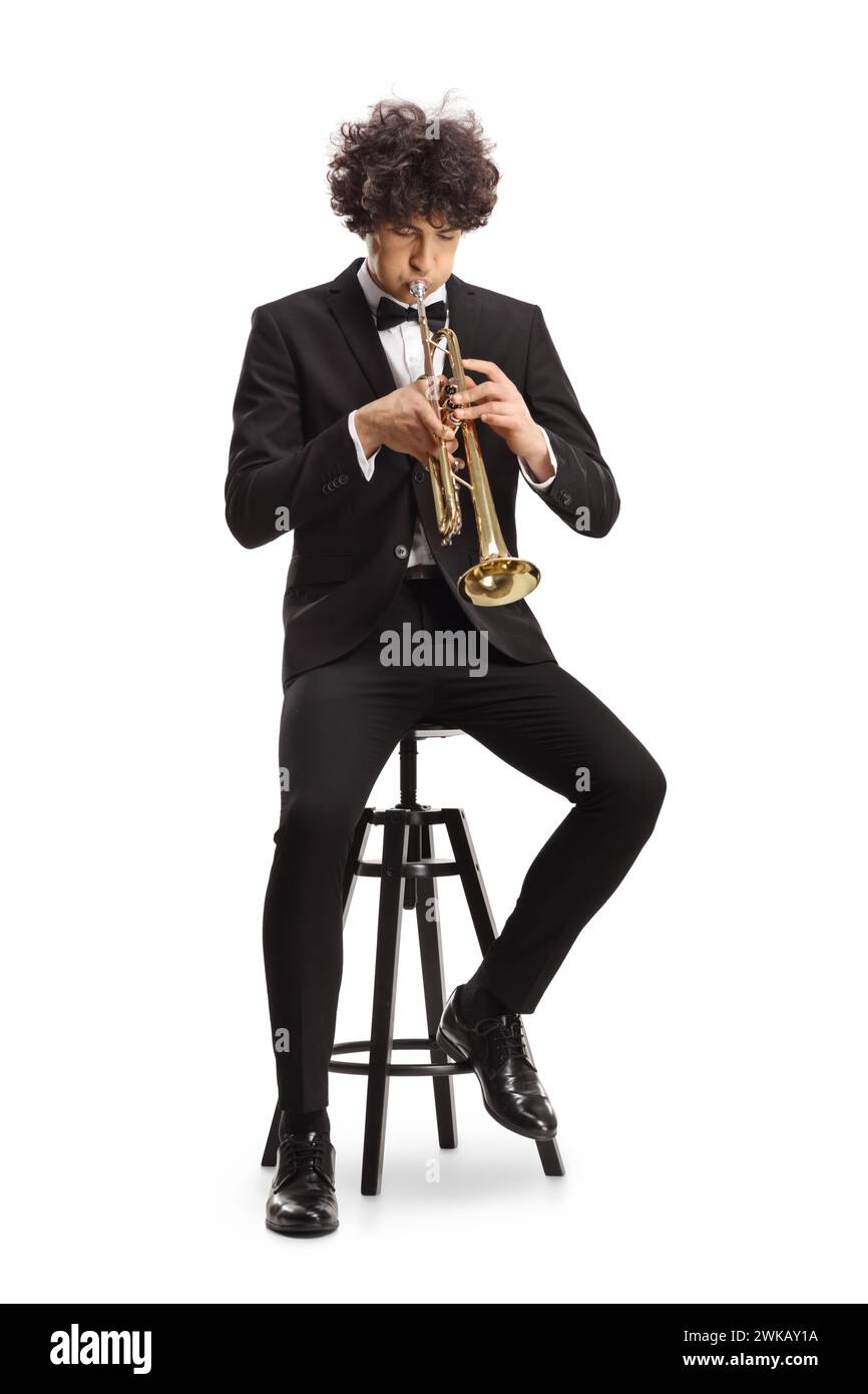 Elegant young man in a black suit playing a trumpet and sitting on a chair isolated on white background Stock Photo