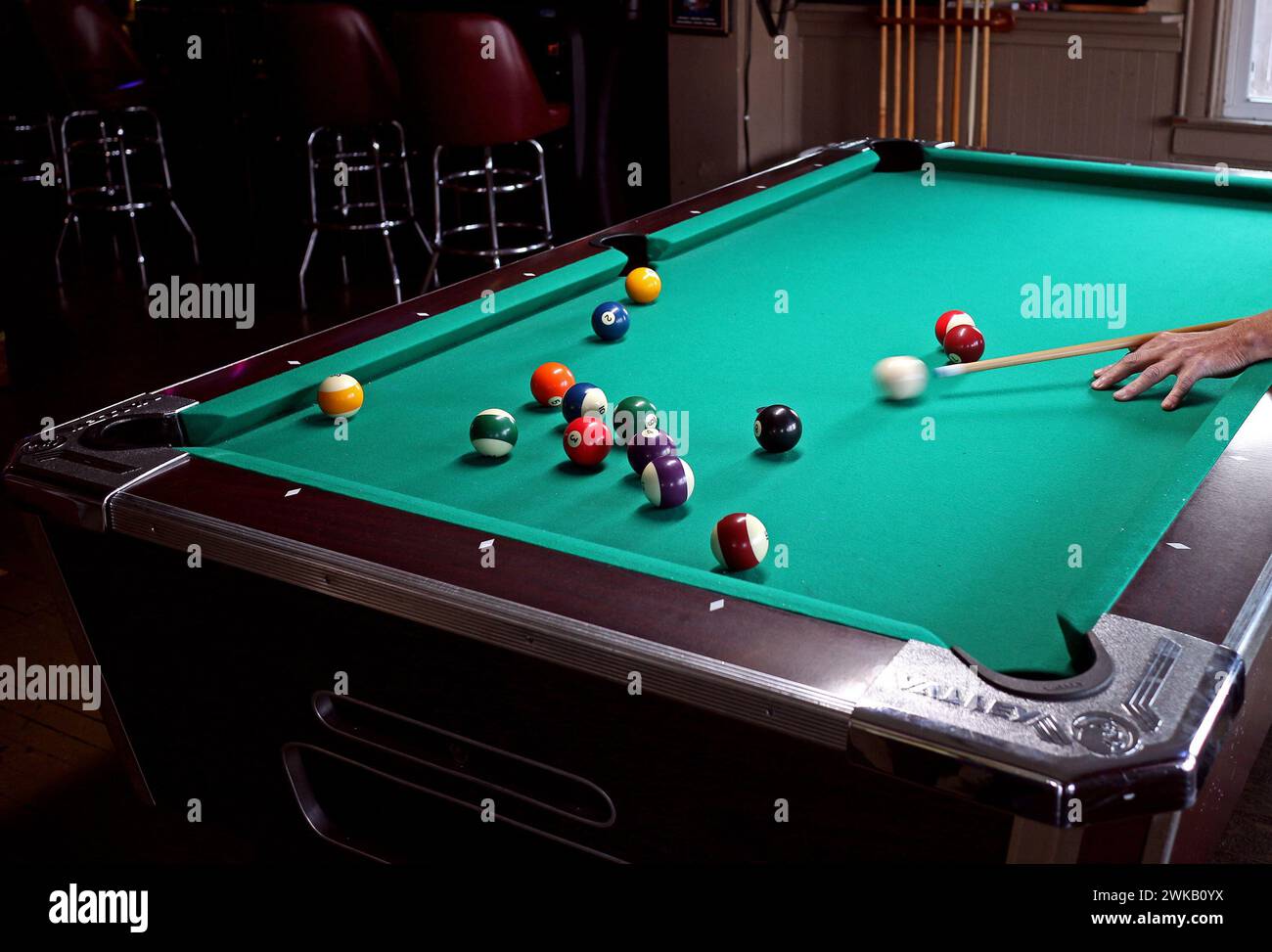 Green pool table in a bar, with a player striking the cue ball towards