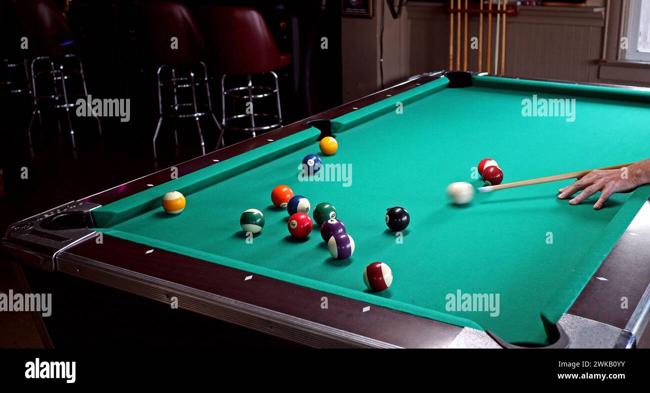 Green pool table in a bar, with a player striking the cue ball towards others. Motion blur of cue stick action. Stock Photo