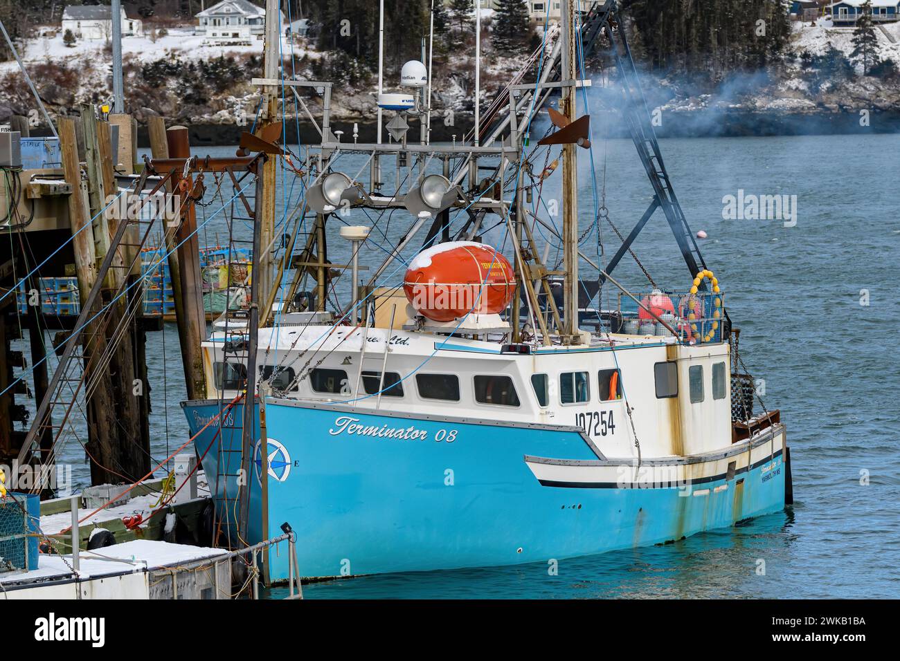Dipper Harbour, NB, Canada - 2024-02-18: A fishing boat docked at low tide. Smoke billows from it as it prepares to sail. Stock Photo
