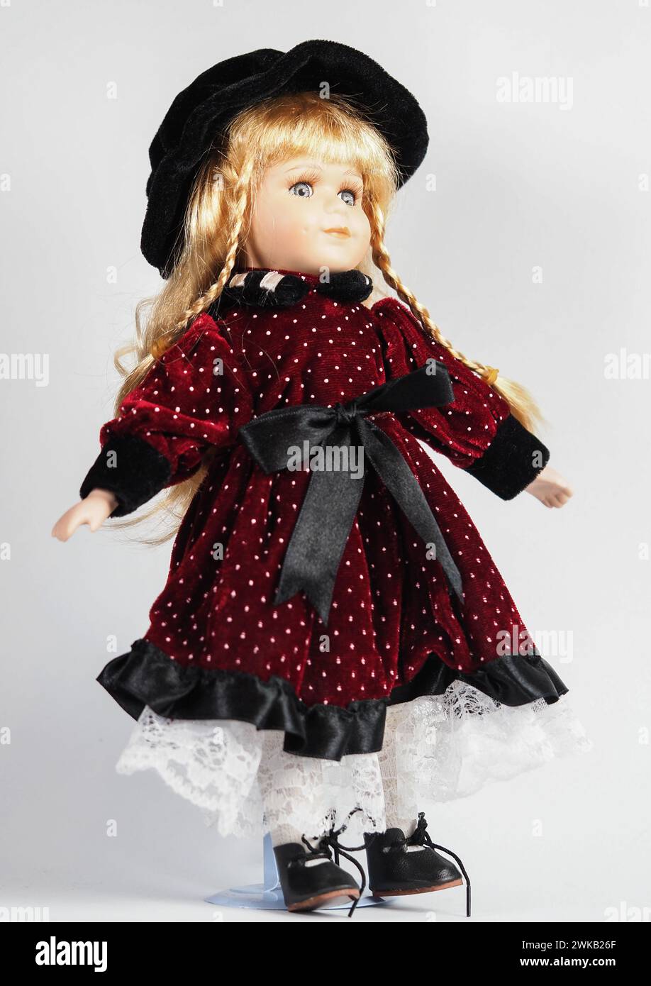 Vintage Austrian porcelain doll girl with blue eyes, blonde with braids, wearing a dark red velvet dress with white polka dots with a black satin belt Stock Photo