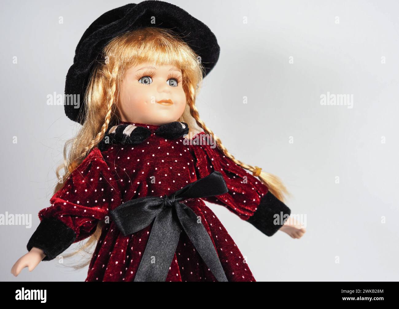 Vintage Austrian porcelain doll girl with blue eyes, blonde with braids, wearing a dark red velvet dress with white polka dots with a black satin belt Stock Photo