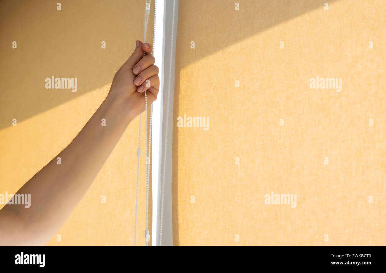 Close-up of a woman's hand opening or closing roller blinds on a sunny day. Stock Photo