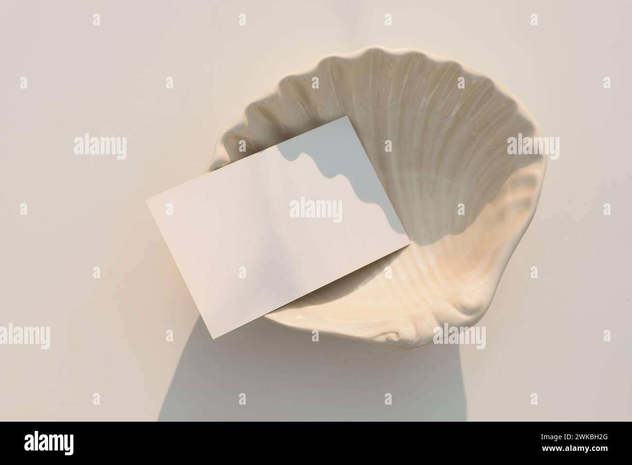 Summer wedding stationery. Blank greeting, RSVP or business card mockup in sunlight. Invitation, template. Beige sea shell plate isolated on table Stock Photo