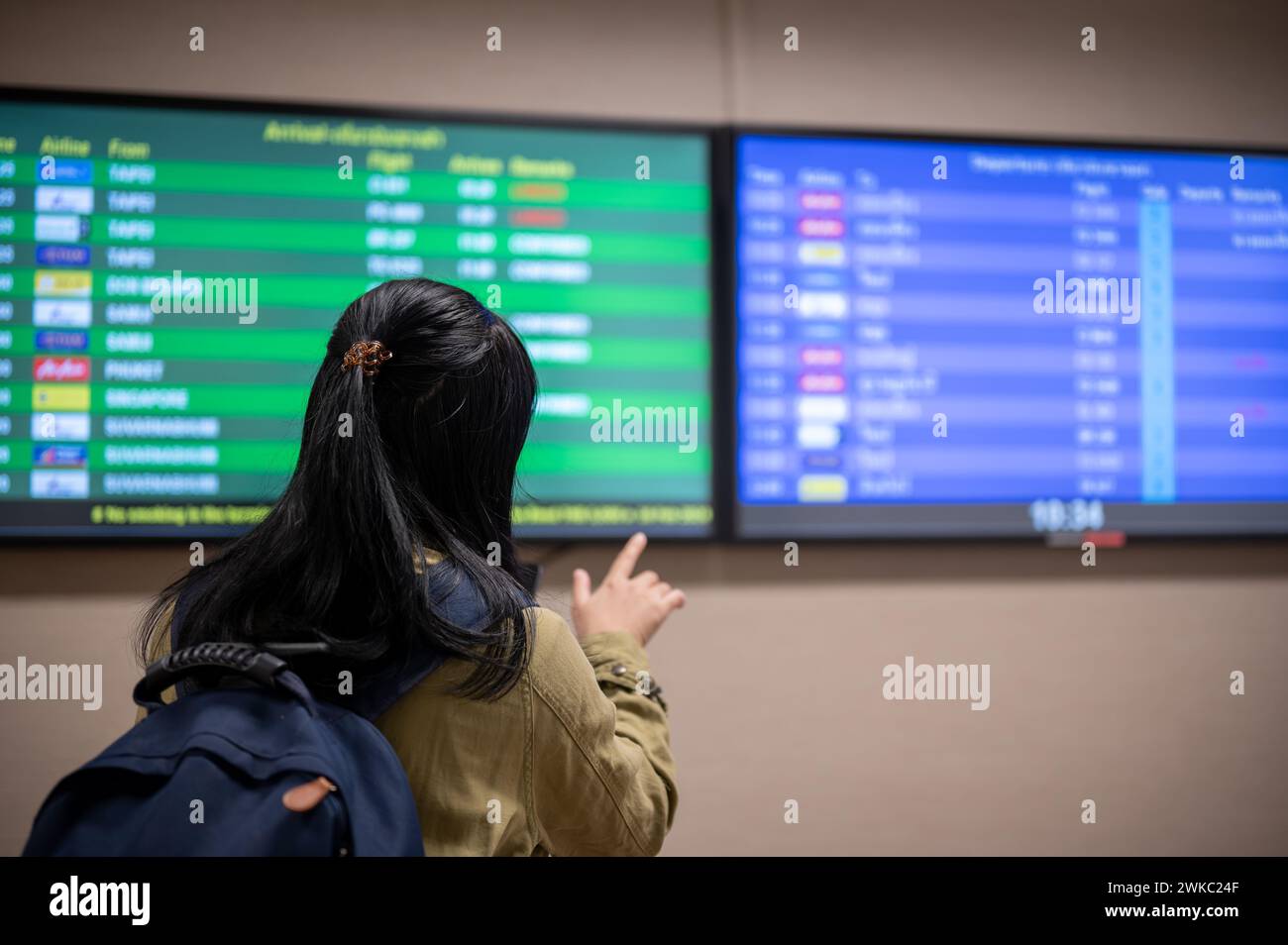 A back view shot of an Asian female passenger checking her boarding time on a monitor screen in the airport. Stock Photo