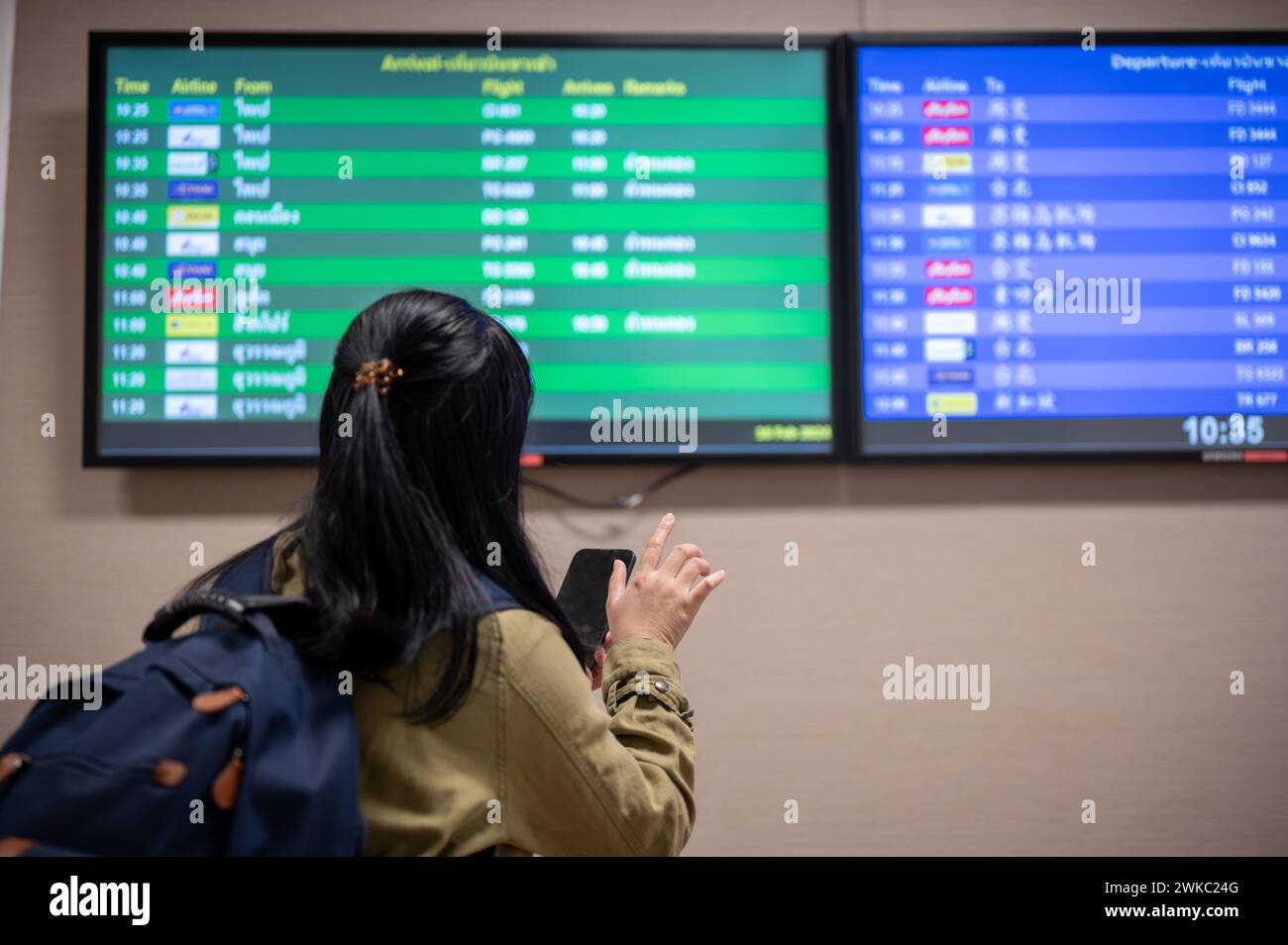 A back view shot of an Asian female passenger checking her boarding time on a monitor screen in the airport. Stock Photo