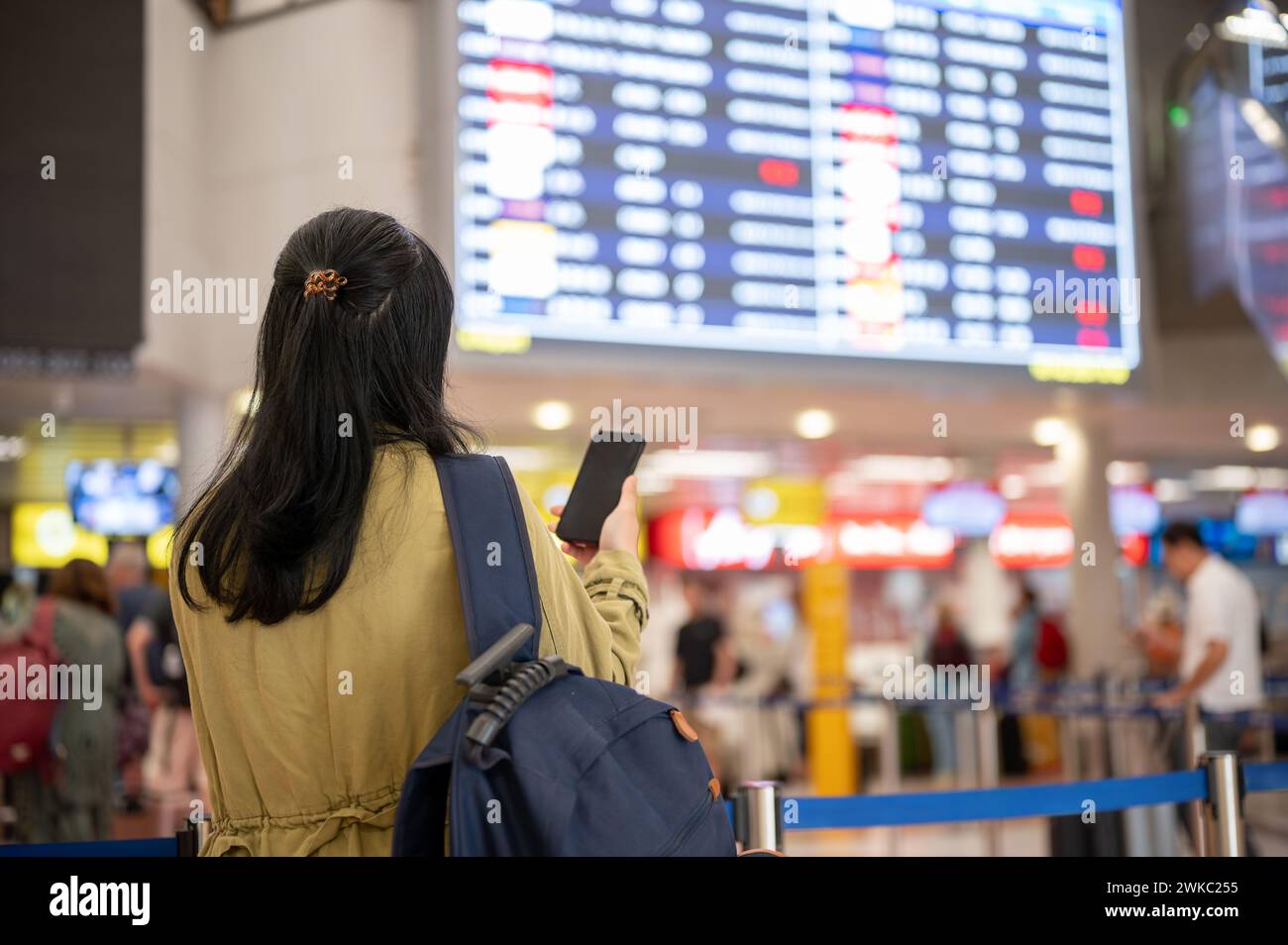 A back view shot of an Asian female traveler or backpacker checking her boarding time on a monitor screen in the airport. Stock Photo