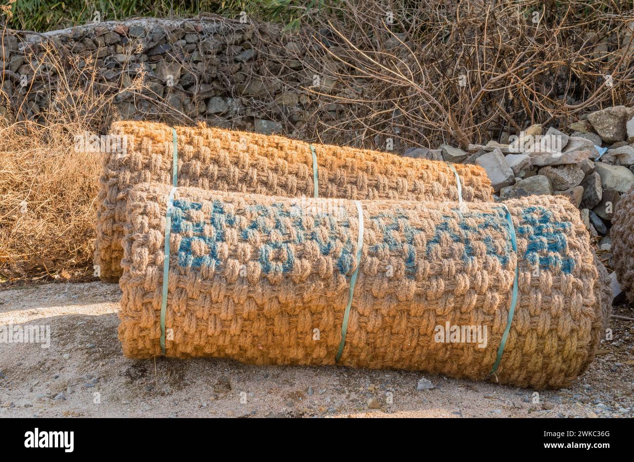 Large trail mats rolled up laying on ground with stone wall in background in South Korea Stock Photo