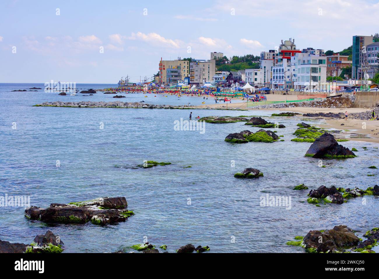 Donghae City, South Korea - July 28th, 2019: Overlooking Eodal Port and Beach, where rocks guard the sandy shores, people enjoy the water shielded by Stock Photo