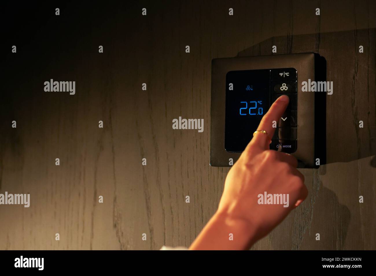A persons hand is seen adjusting a digital smart thermostat to maintain