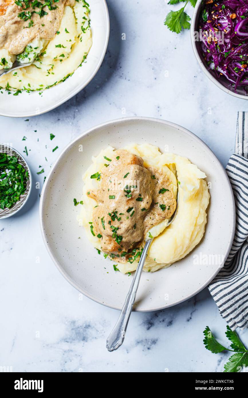 Chicken breast in creamy sauce with mashed potatoes, top view,  white marble background. Stock Photo