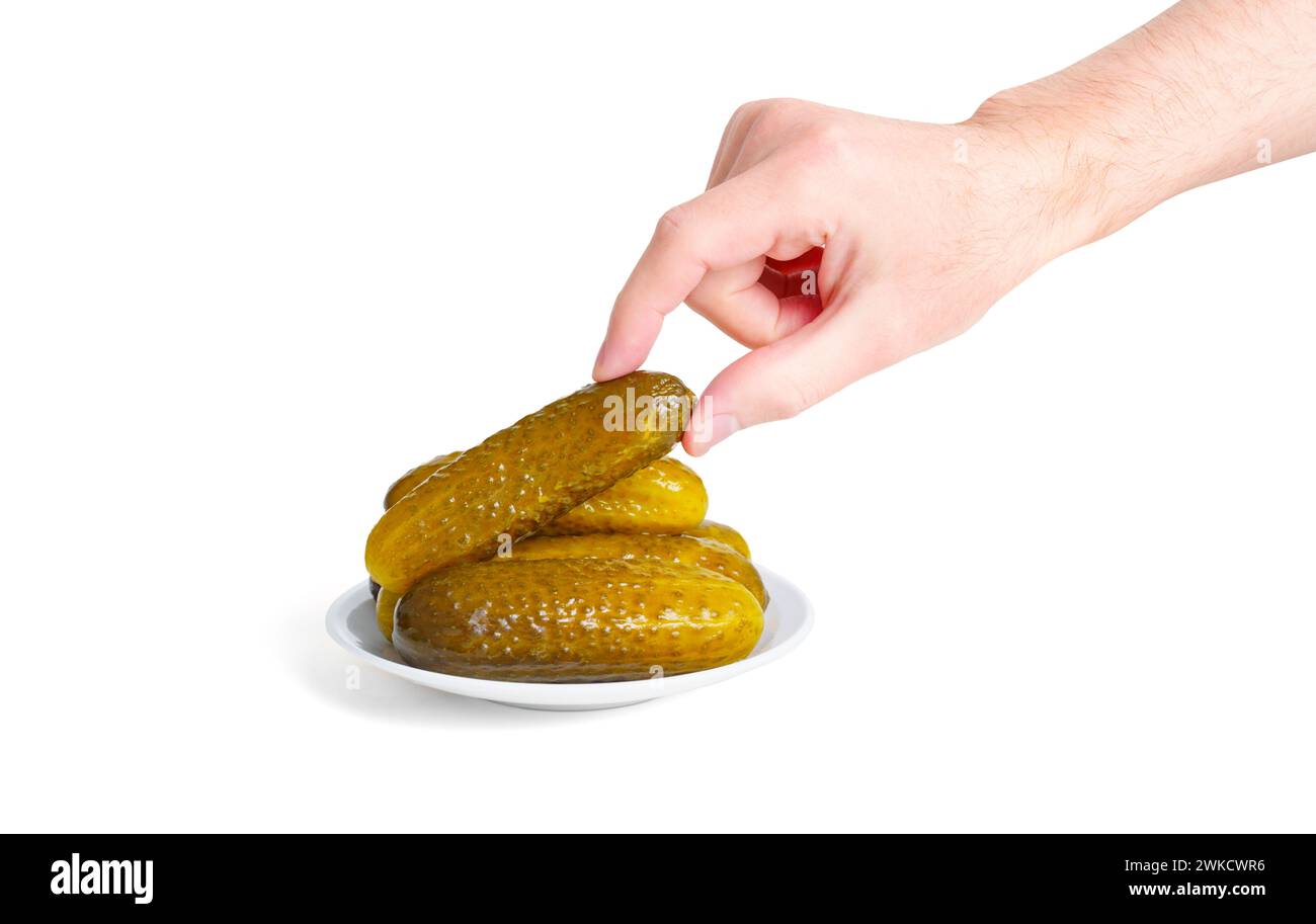 Male hand gracefully takes a pickled cucumber from a plate, set against a pristine white background. Stock Photo