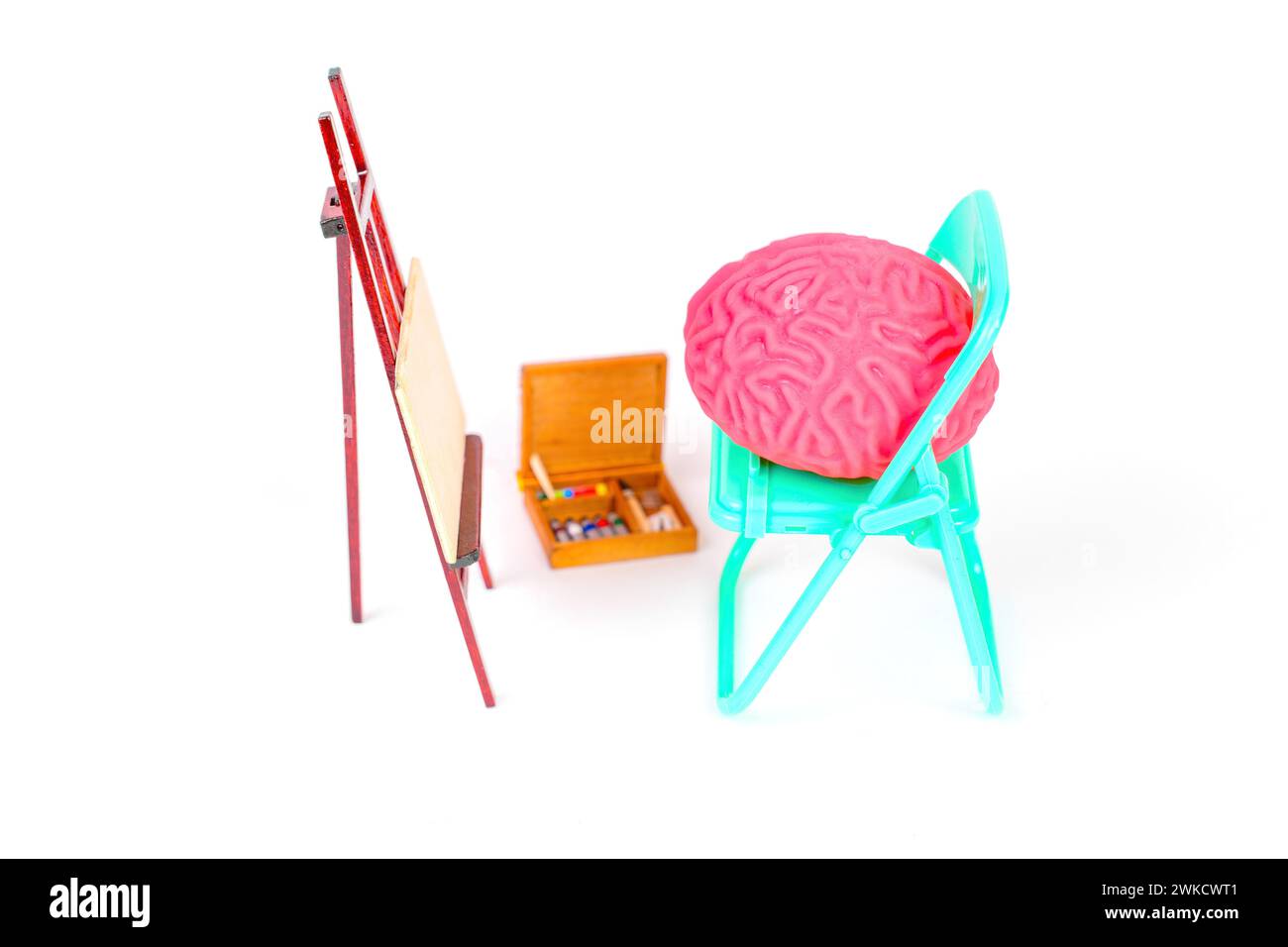 Human brain model seated on a folding teal chair beside an easel, accompanied by a box of vibrant paints. Artificial Intelligence and digital art conc Stock Photo
