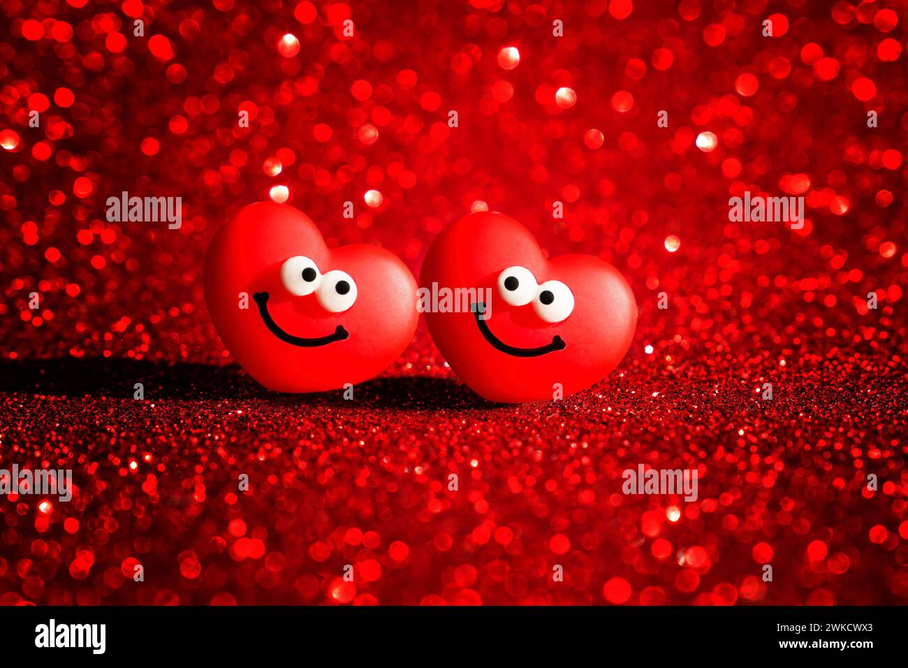 Two smiling heart characters radiate joy on a sparkling red backdrop, creating the perfect Valentine's Day card. Stock Photo