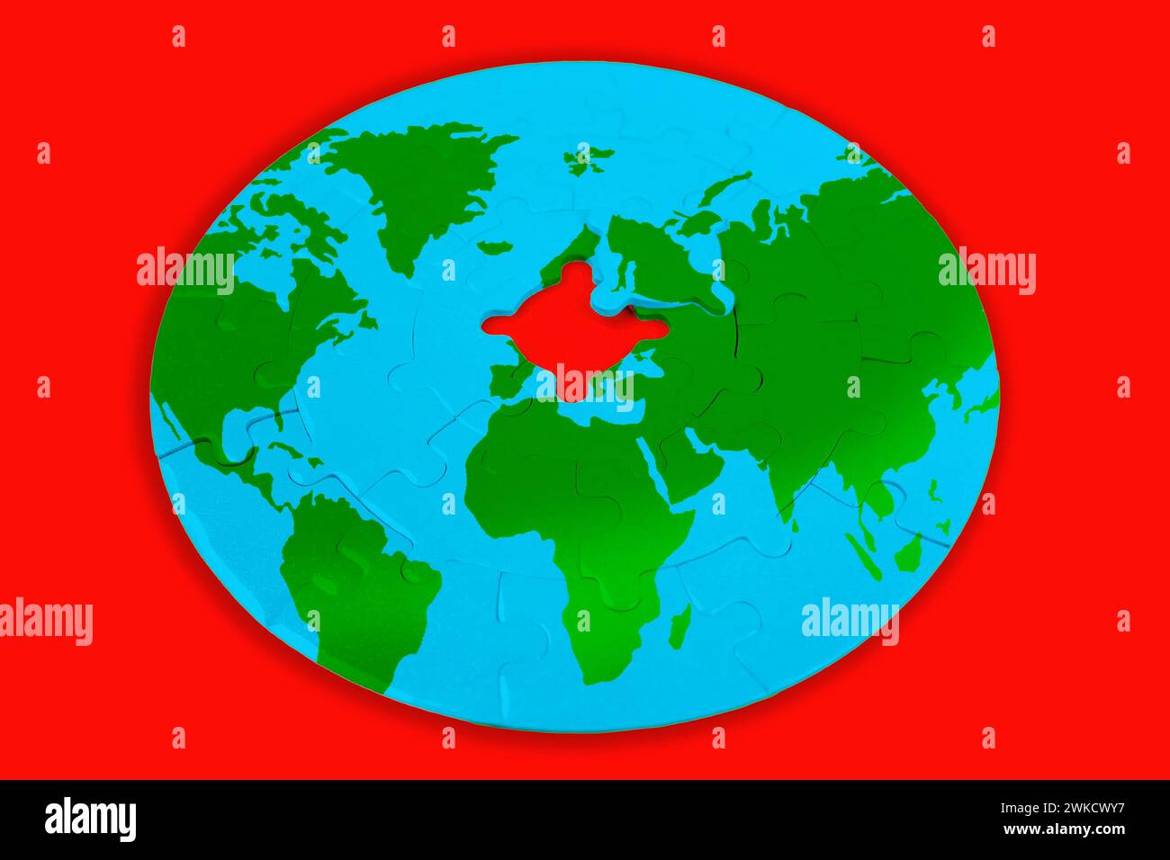 Round jigsaw puzzle depicts a world map with green continents and blue oceans on a red background, with the missing center piece. Global unity and coo Stock Photo
