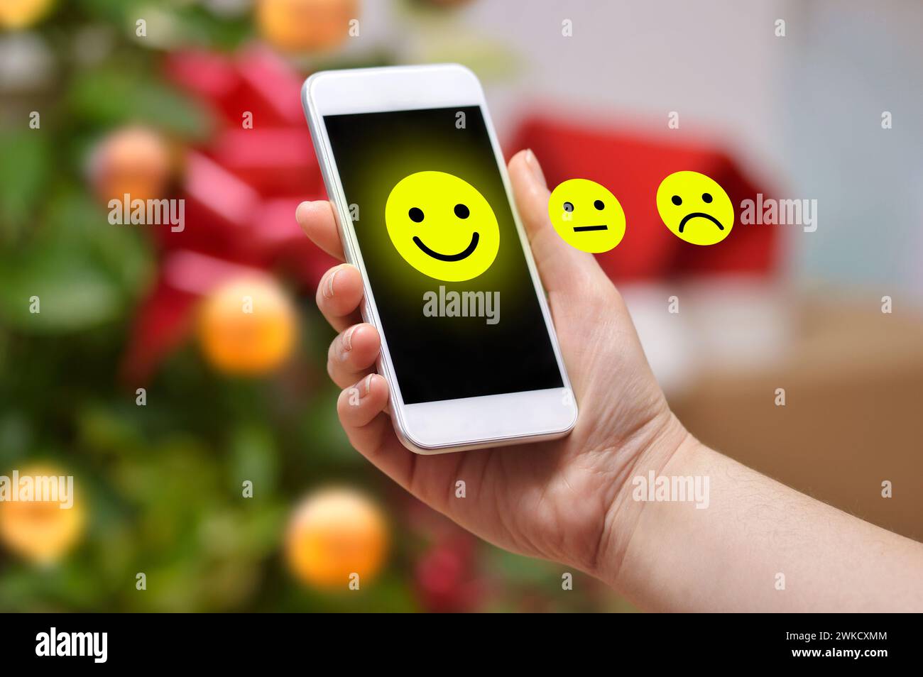 Close up hand of a woman holding a phone with an icon smiling at home on Christmas day Stock Photo