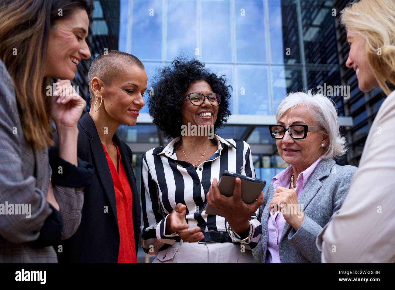 Team diverse ages and race business women talking about commerce looking and using tablet outdoors. Stock Photo