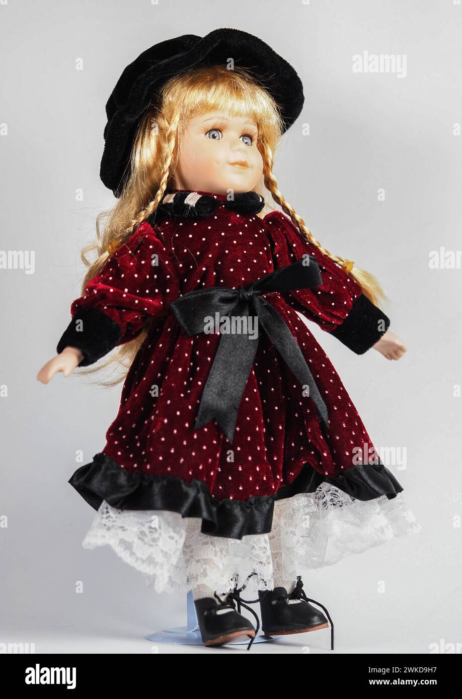 Garham, Germany. 19th Feb, 2024. Vintage Austrian porcelain doll girl with blue eyes, blonde with braids, wearing a dark red velvet dress with white polka dots with a black satin belt and a black hat. Porcelain dolls appeared in the 18th century in France. Credit: SOPA Images Limited/Alamy Live News Stock Photo