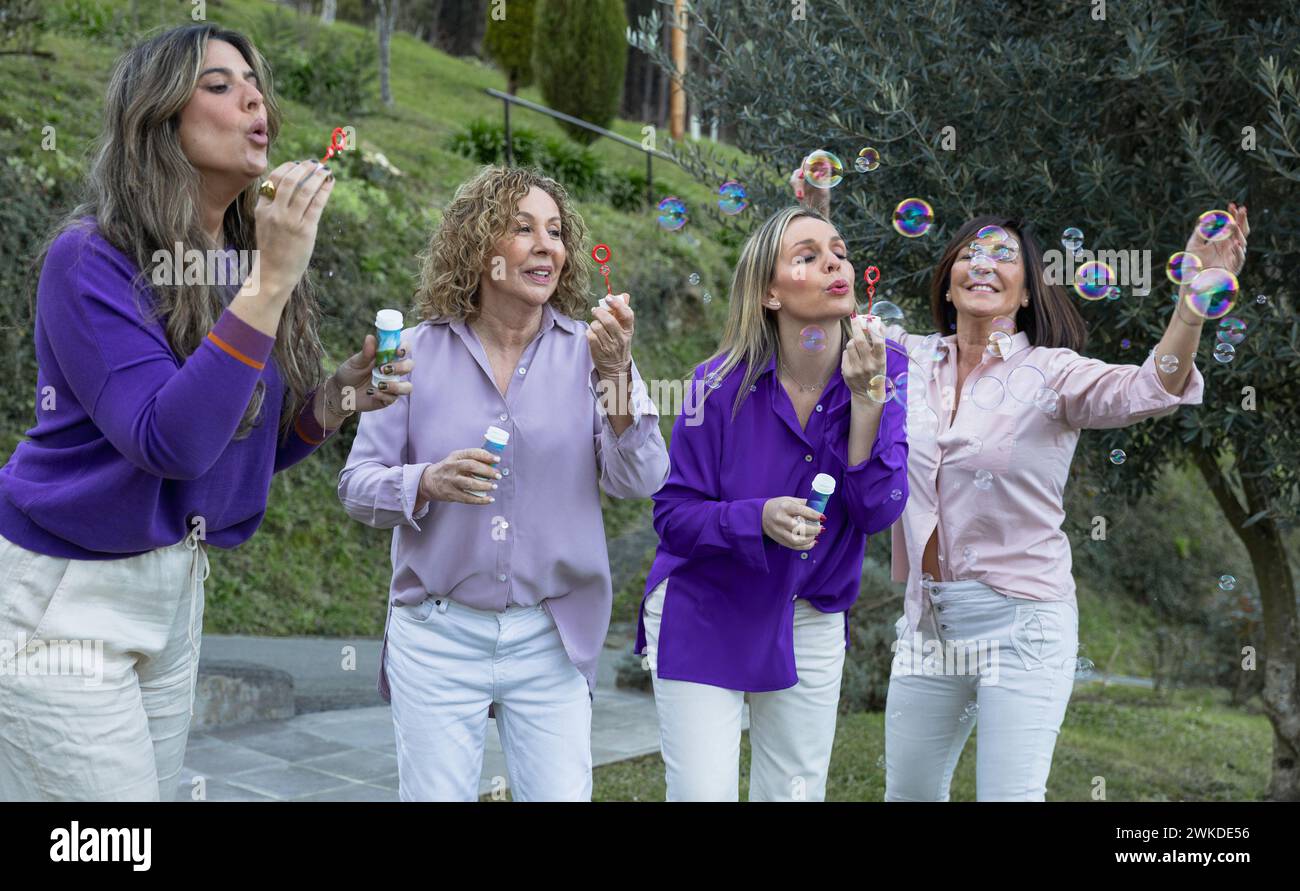 A playful and joyous scene of women in vibrant blouses blowing bubbles, enjoying a lighthearted moment together in an outdoor setting. Stock Photo