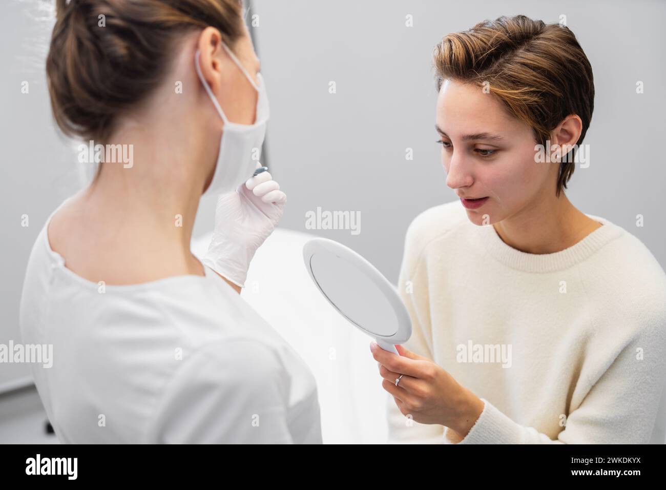 A young woman looks at her face after procedures in a beauty salon. Stock Photo