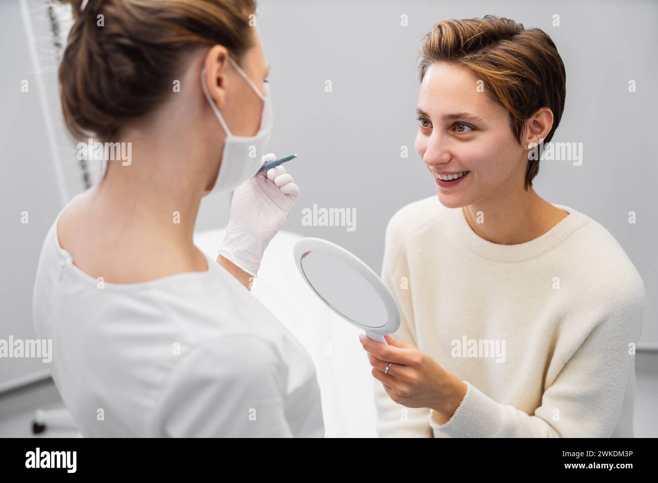 A young woman looks at her face after procedures in a beauty salon. Stock Photo