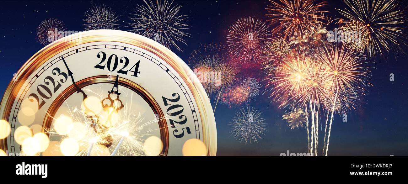 Vintage gold clock hands point to New Year 2024 on the night sky with fireworks and sparklers. New Year Eve celebration Stock Photo