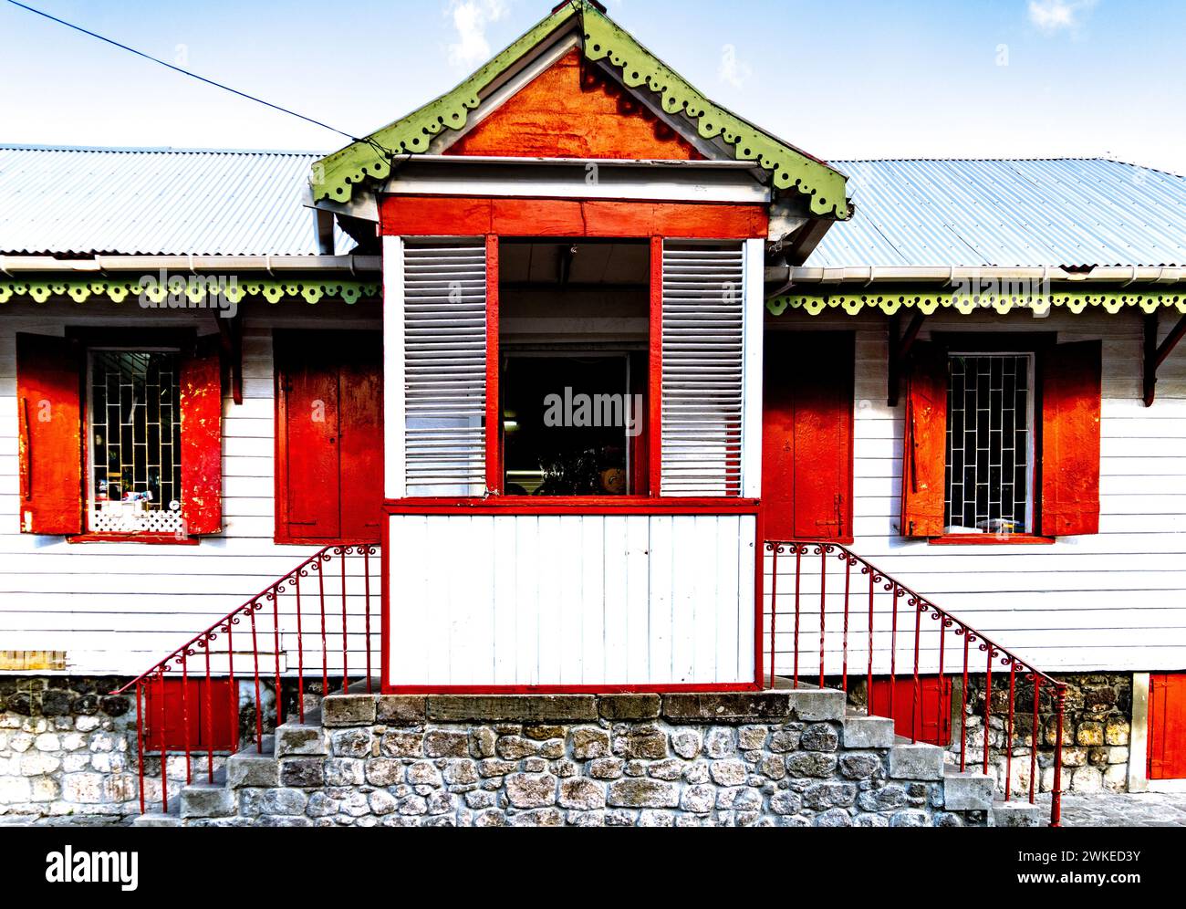 A wooden house with red frames and green rooftop in Dominica Stock Photo
