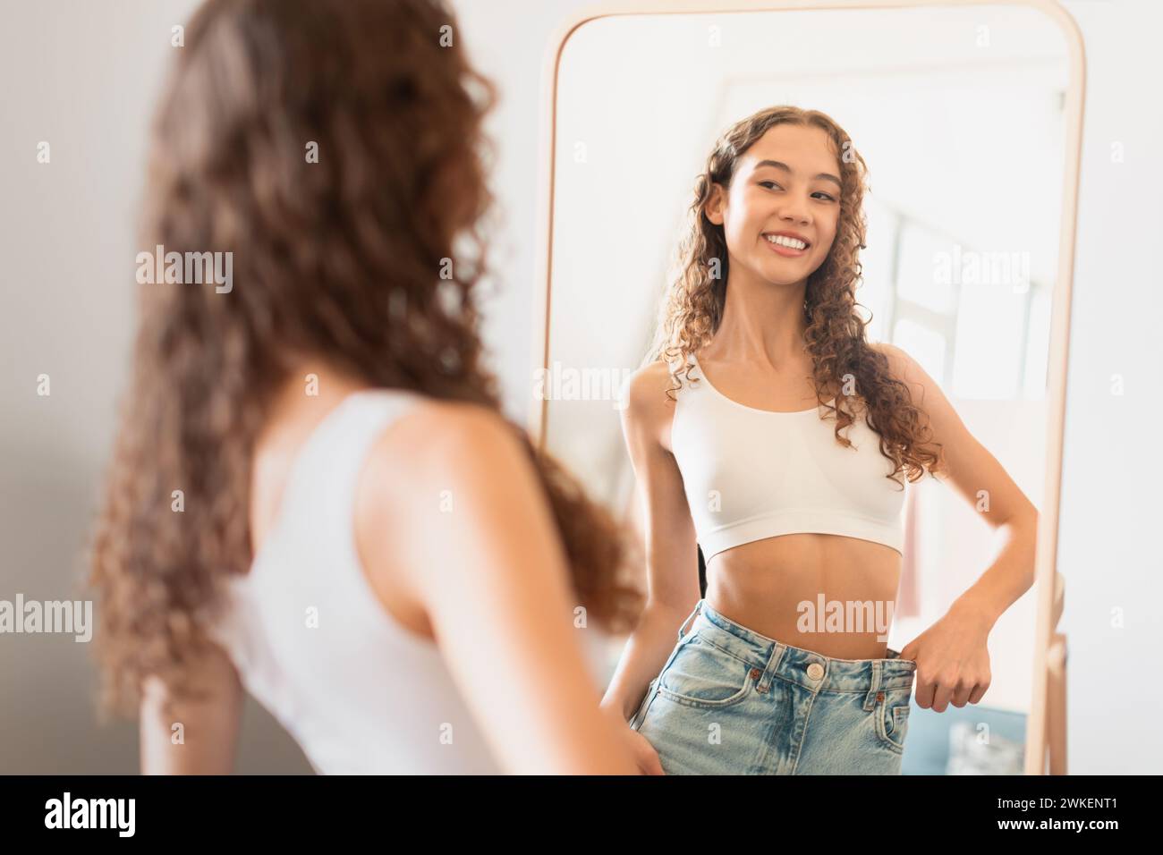 teen girl looks at mirror satisfied with weight loss indoor Stock Photo