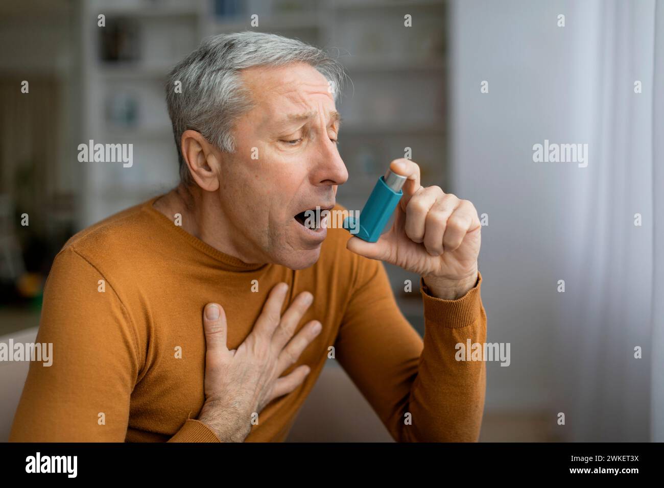 Sick grey-haired senior man touching chest and using asthma inhaler Stock Photo