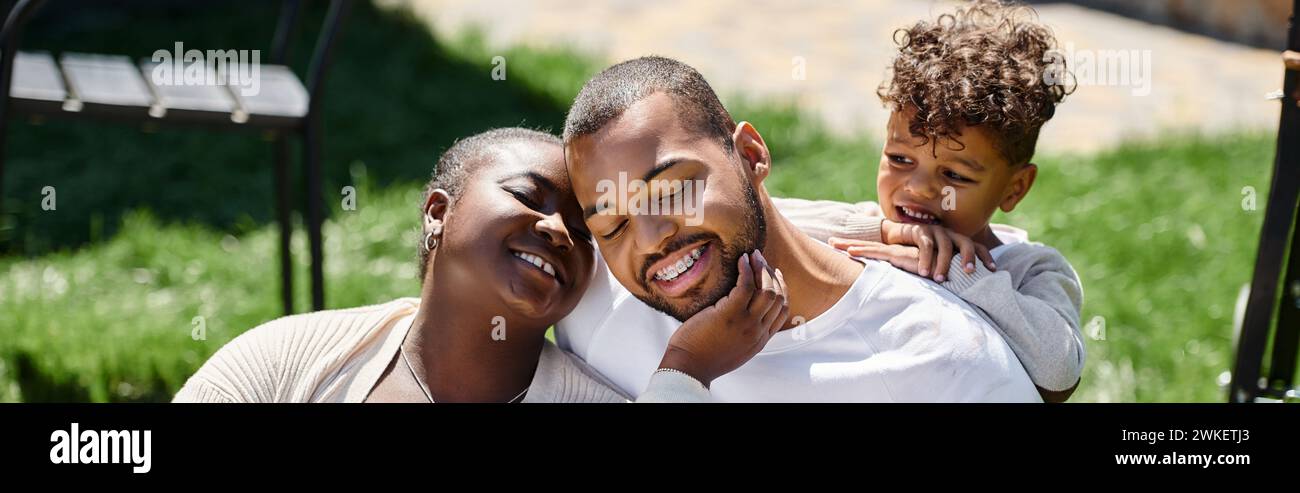 family moment of happy african american parents and son smiling and sitting on green lawn, banner Stock Photo