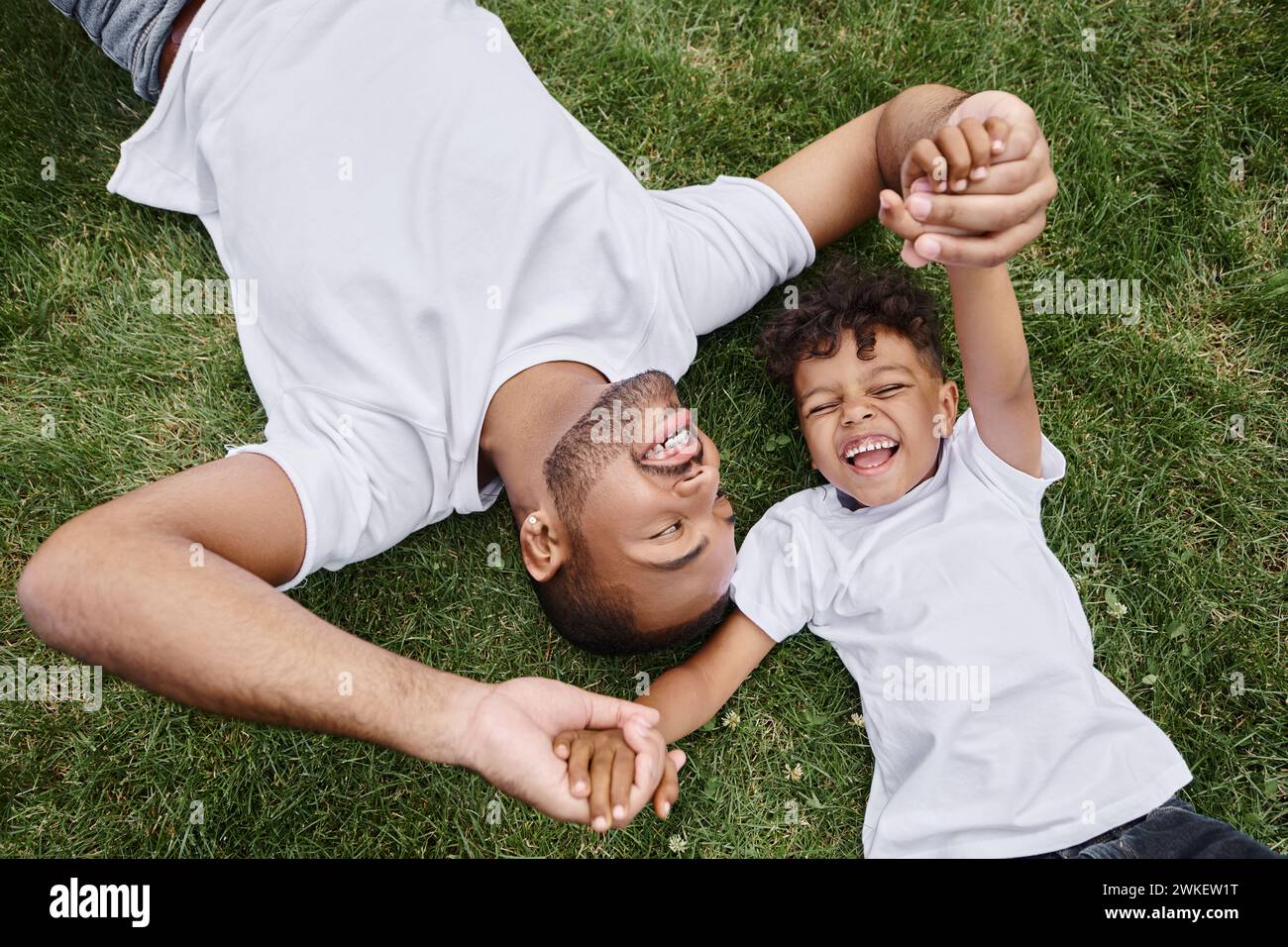 top view of happy african american father and son lying on lawn on ...