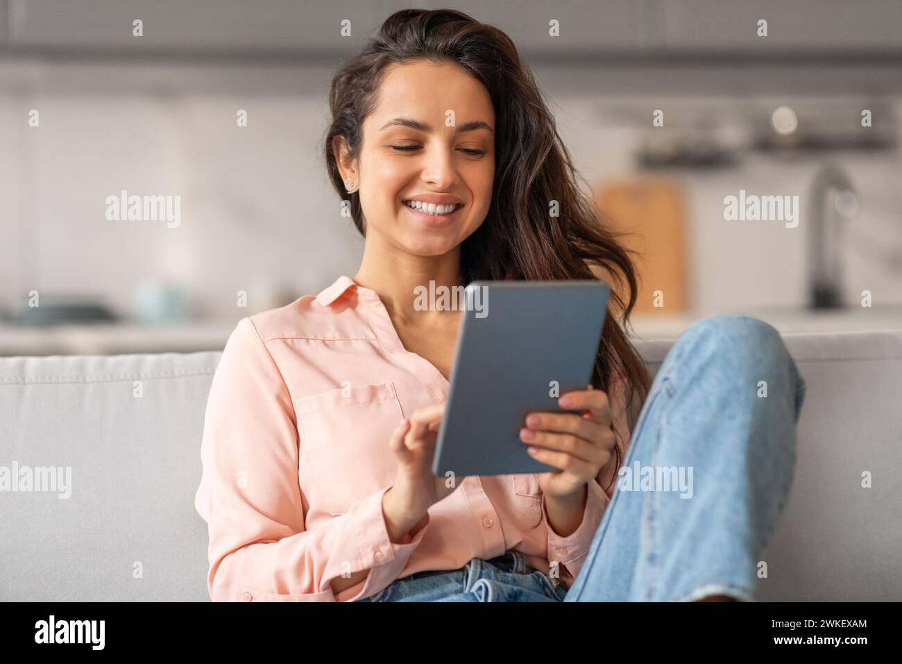 Happy woman using tablet on sofa at home Stock Photo