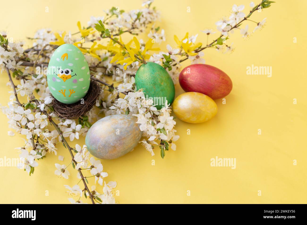 Colorful Easter eggs with white flowering twigs on a yellow background Stock Photo