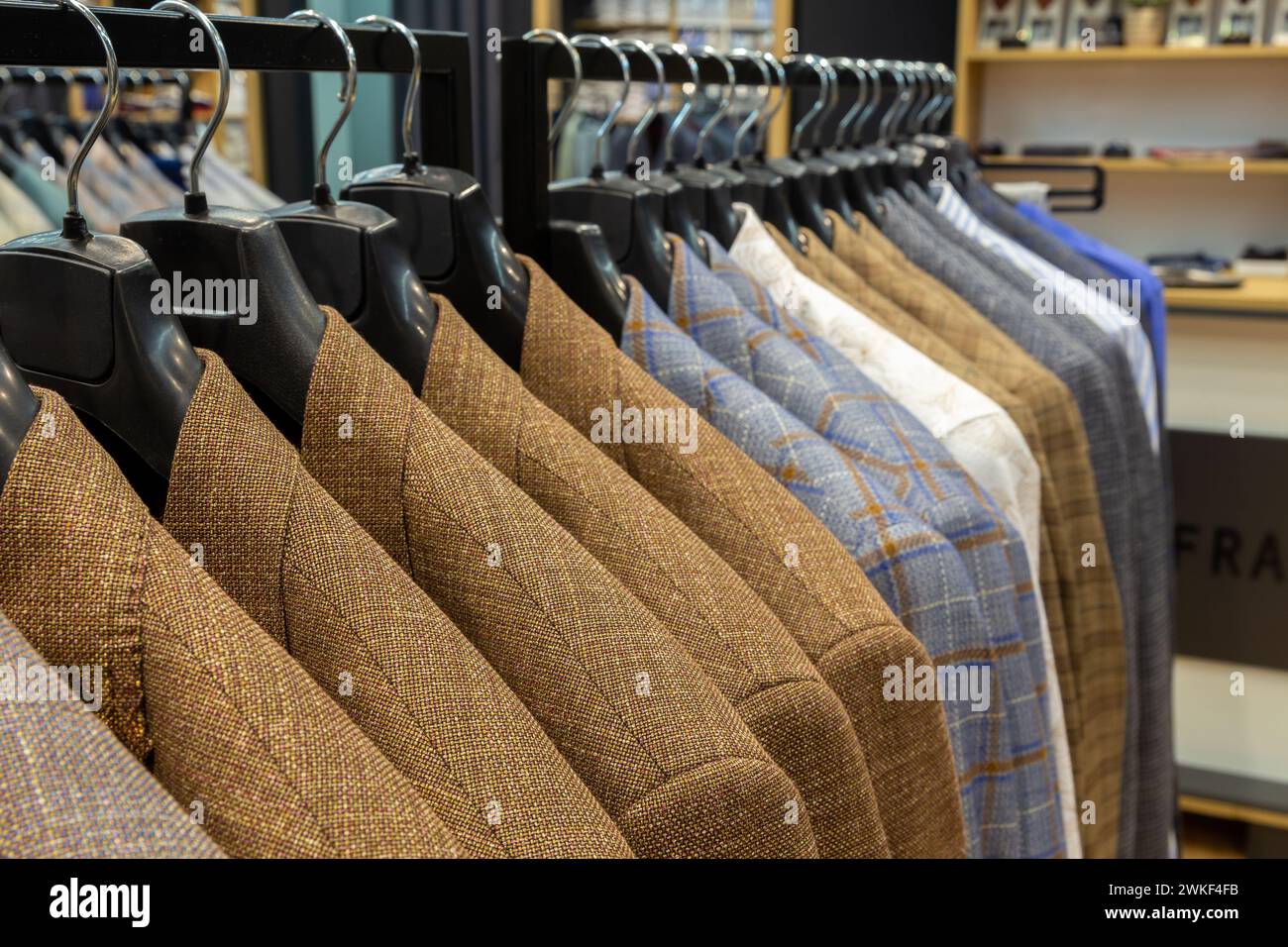A row of men's suits, jackets hanging on a rack for display. Elegant man suit jackets hanging in a row on hangers. Stock Photo