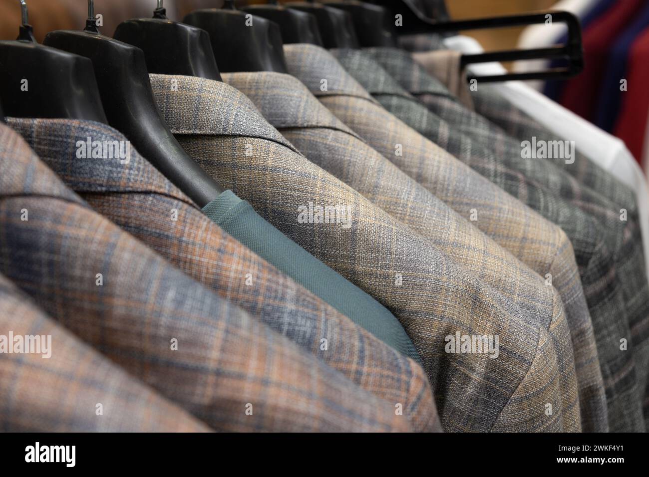 A row of men's suits, jackets hanging on a rack for display. Elegant man suit jackets hanging in a row with close up of sleeve and buttons. Stock Photo