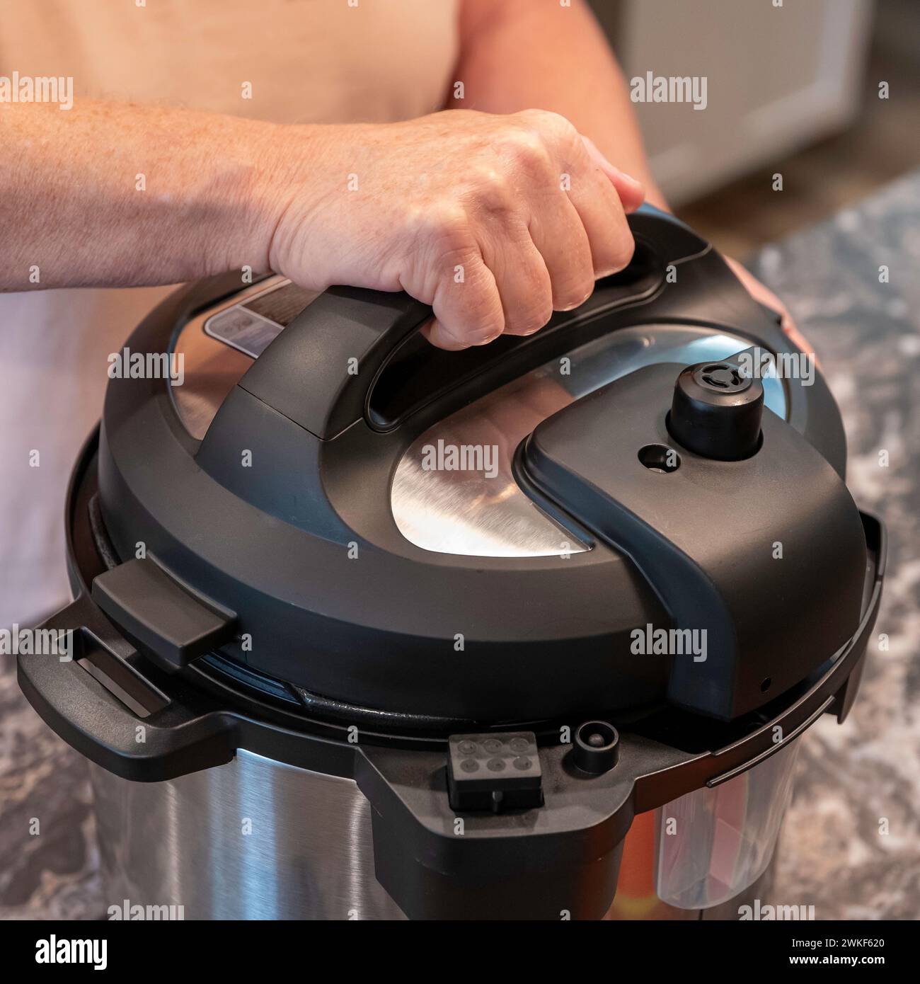 Fingers of a womans hand are curled around the handle of the cover of a modern electric pressure cooker or instant pot. Stock Photo