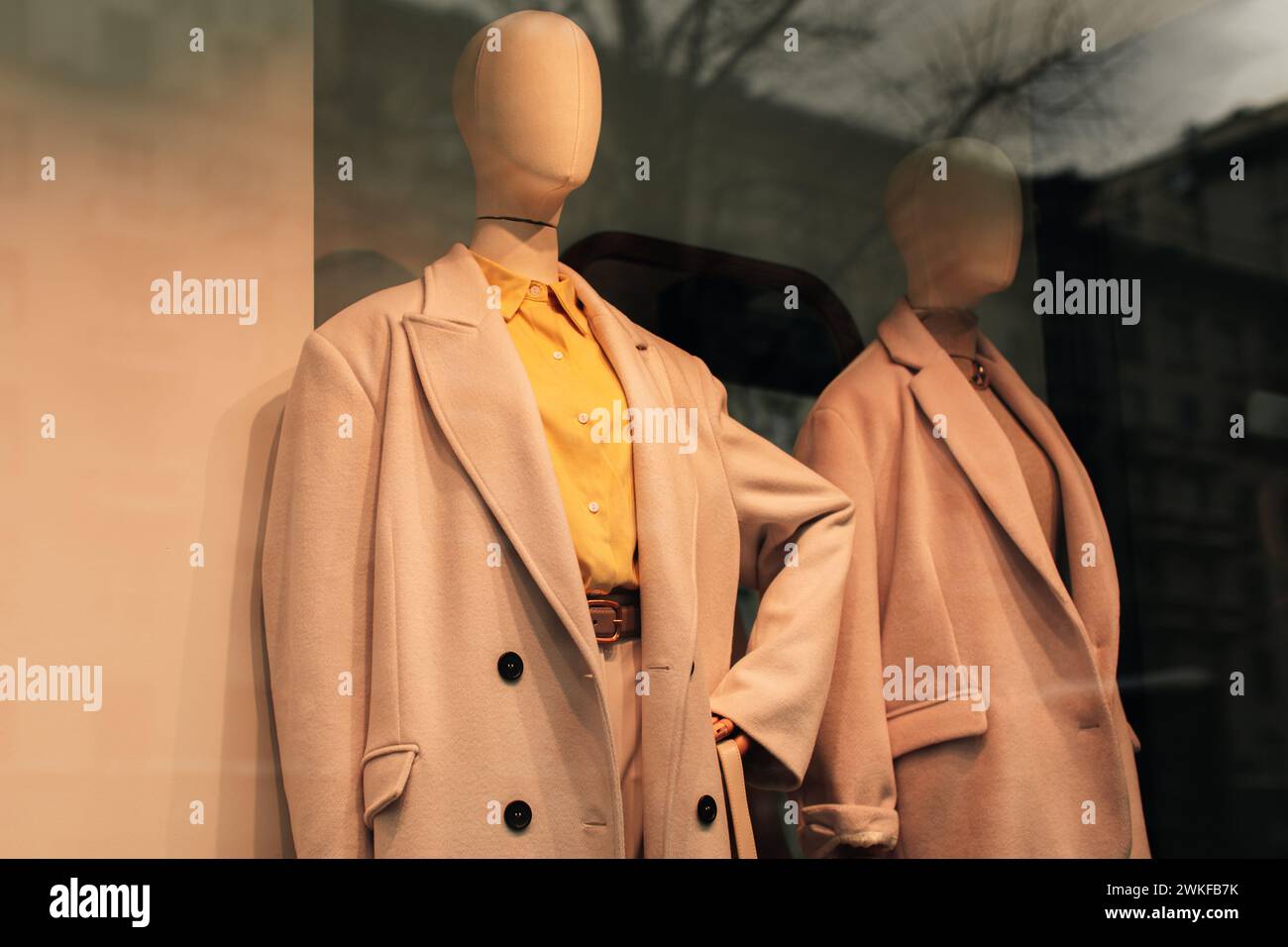 Mannequins in a store window dressed in seasonal fashion. Beige coat and a bright yellow shirt. Stock Photo