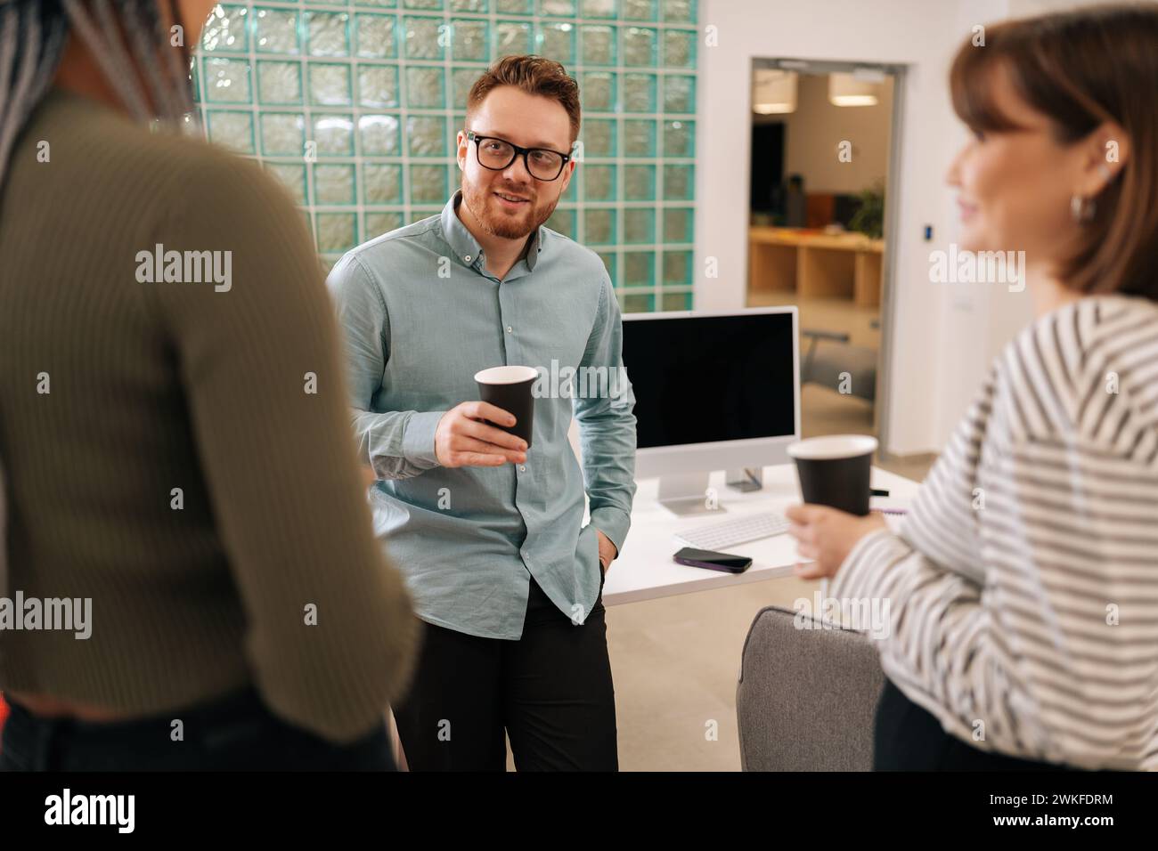 Happy group of ethnically diverse young man and women relaxing while having coffee break at work in light modern office room. Relaxed coworkers Stock Photo