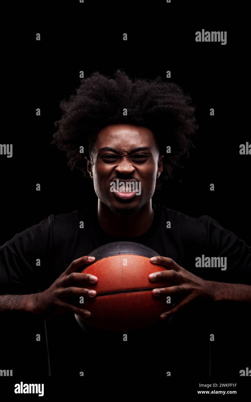 Basketball player holding a ball against black background and screaming