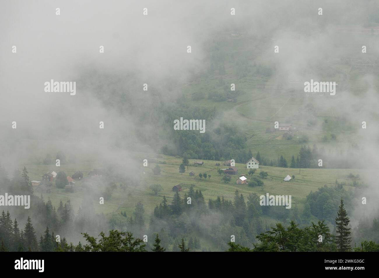 Dense fog in the mountains, through which houses and the village are barely visible, morning haze in the mountains. Stock Photo
