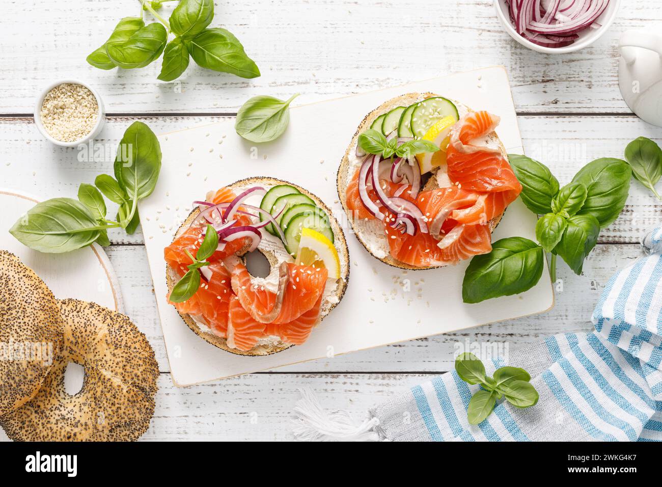 Salmon sandwiches with bagel, salted fish, fresh cucumber, onion and basil on white background, top view. Healthy breakfast with salmon toasts Stock Photo