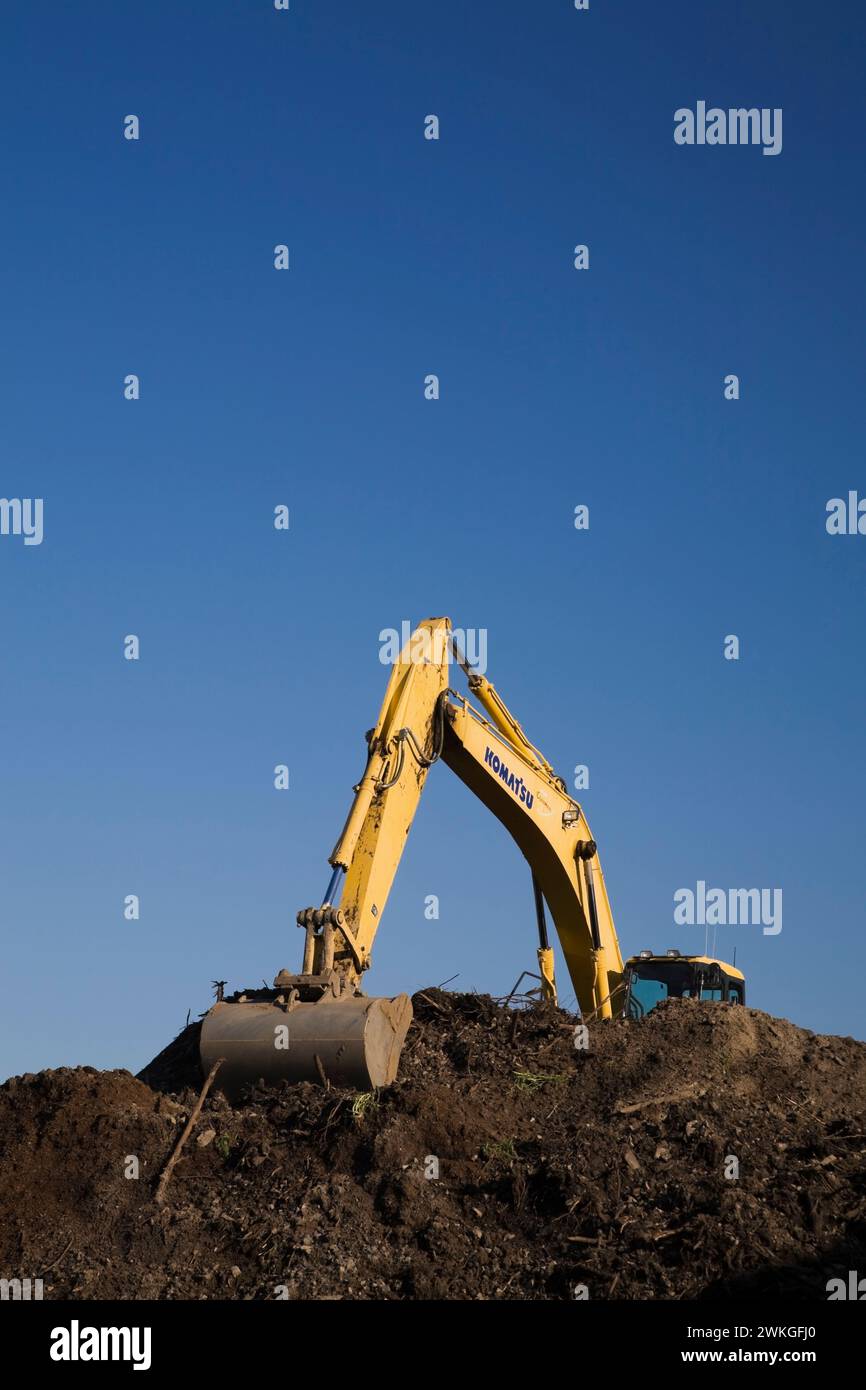 Komatsu excavator with scooping bucket on top of mound of brown topsoil