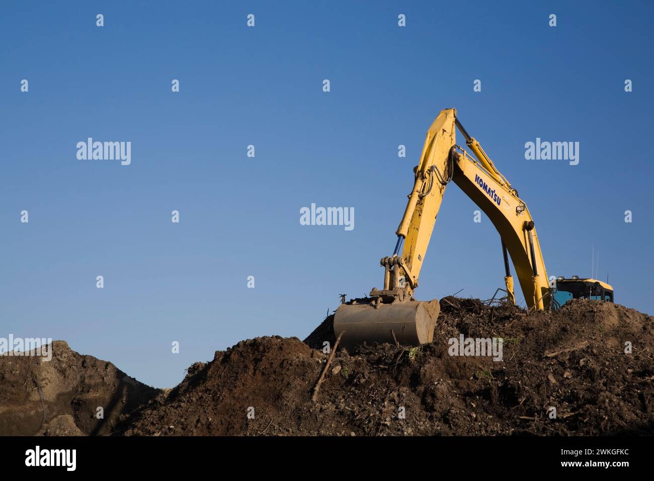 Komatsu excavator with scooping bucket on top of mound of brown topsoil