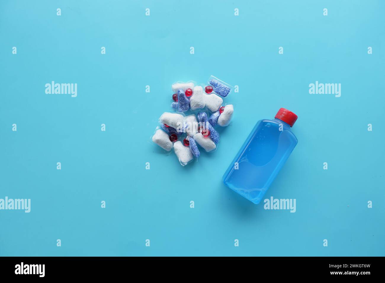 A stack of dishwasher tablets and a bottle of detergent on a blue background Stock Photo