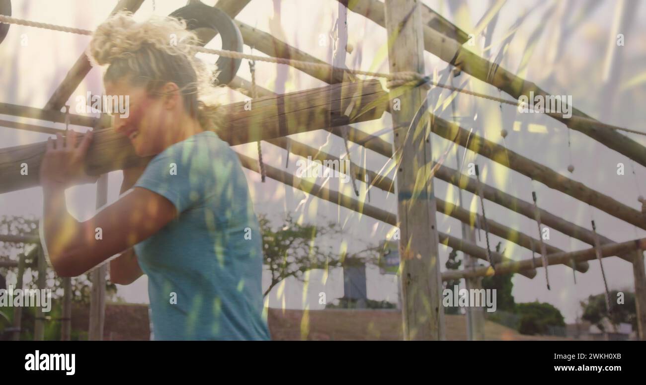 Image of grass over diverse women at obstacle course carrying wooden bars Stock Photo